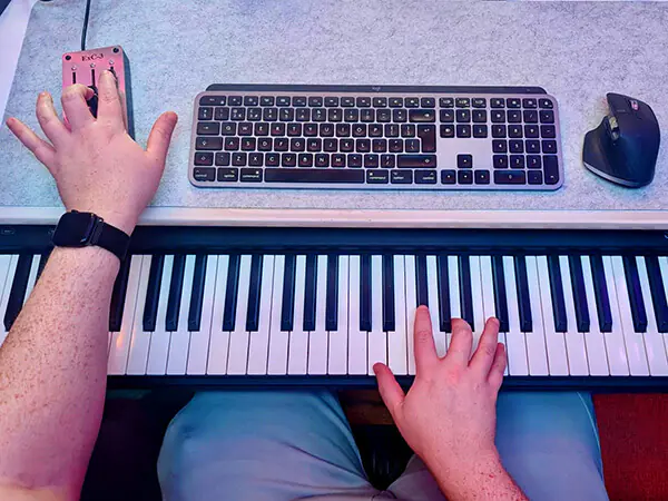 A composer's-eye view of the desktop featuring a digital piano, MIDI controllers, keyboard and mouse.